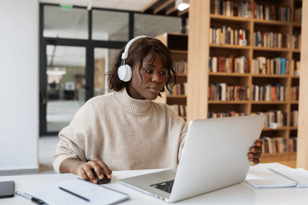 Uma mulher estudando em um site para estudar para o Enem em seu computador, em uma biblioteca.